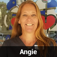 A woman with long red hair smiles at the camera. She is wearing a dark top and standing in front of a window with colorful shapes and designs. The name "Angie, Veterinarian" is displayed in white text on a black bar at the bottom of the image.